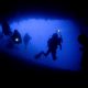 Advanced scuba divers with dive lights exploring the famous Turtle Tomb, an underwater cavern system with lost turtle skeletons at Sipadan Island.