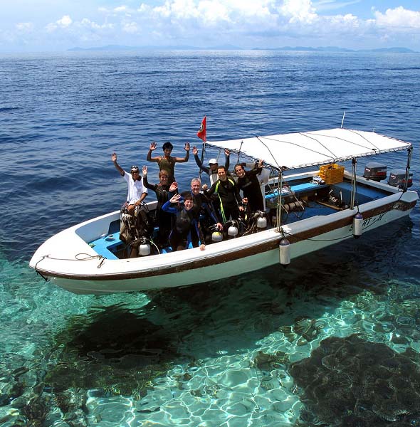Happy group of divers in full scuba gear waving from a dive boat, ready for an exciting day of diving at Sipadan with Mabul Water Bungalows.