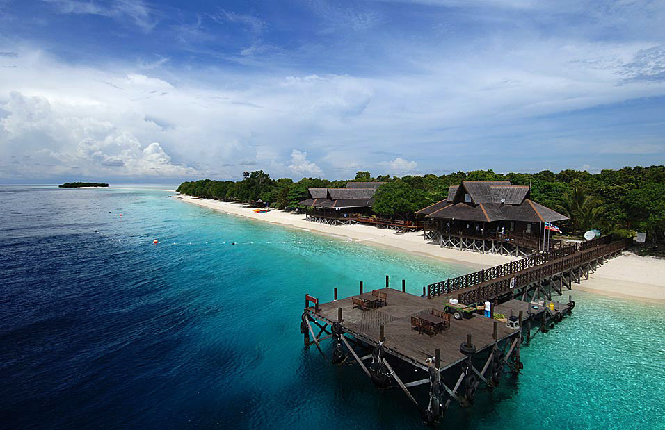 Aerial view of the arrival jetty at Mataking Island Dive Resort, with dive boats moored in turquoise water next to the perfect white sand beach.