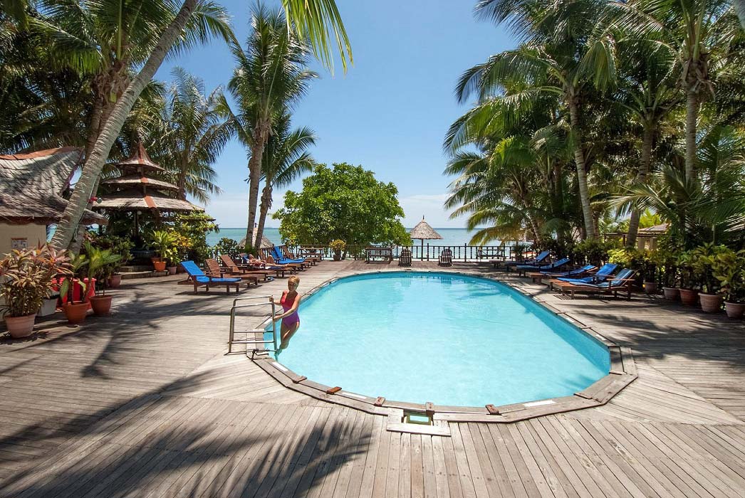 Refreshing swimming pool at Sipadan-Mabul Resort, surrounded by a wooden sundeck and palm trees with a view of the sea.