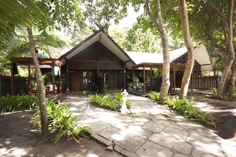 The exterior view of a Deluxe Room building at Mataking Island Resort, surrounded by lush tropical gardens and trees.