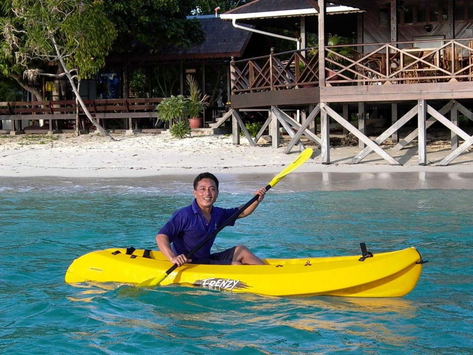 Guest enjoying a peaceful paddle in a kayak on the calm, turquoise sea in front of the Mataking Island Resort.