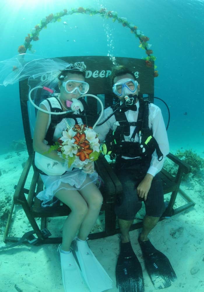 Adventurous couple in full scuba gear celebrating their unique underwater wedding with Mataking resort, complete with a bridal bouquet and a floral arch on the seabed.