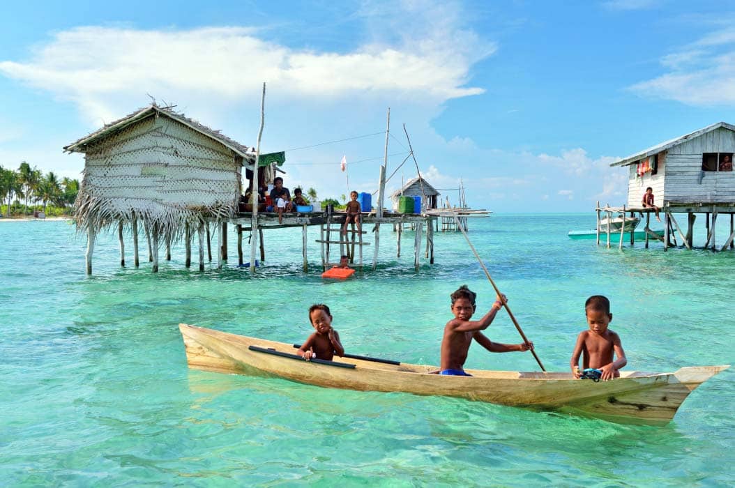 Local children playing in a traditional dugout canoe in their village on Mabul Island, showcasing the Bajau Laut way of life.