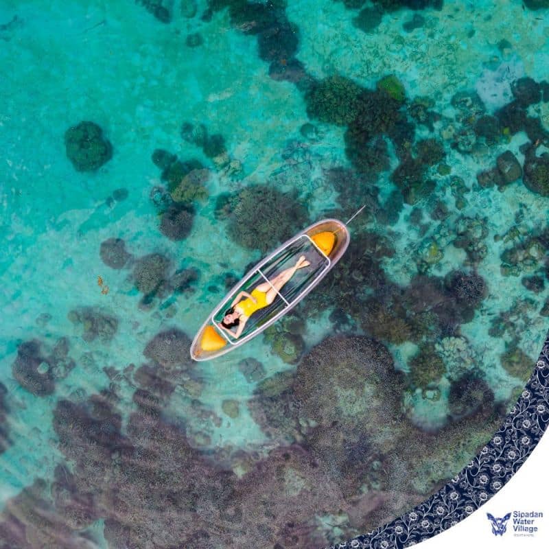 Guest relaxing in a transparent kayak, looking down at the beautiful coral reef below in the crystal-clear waters of Sipadan Water Village.