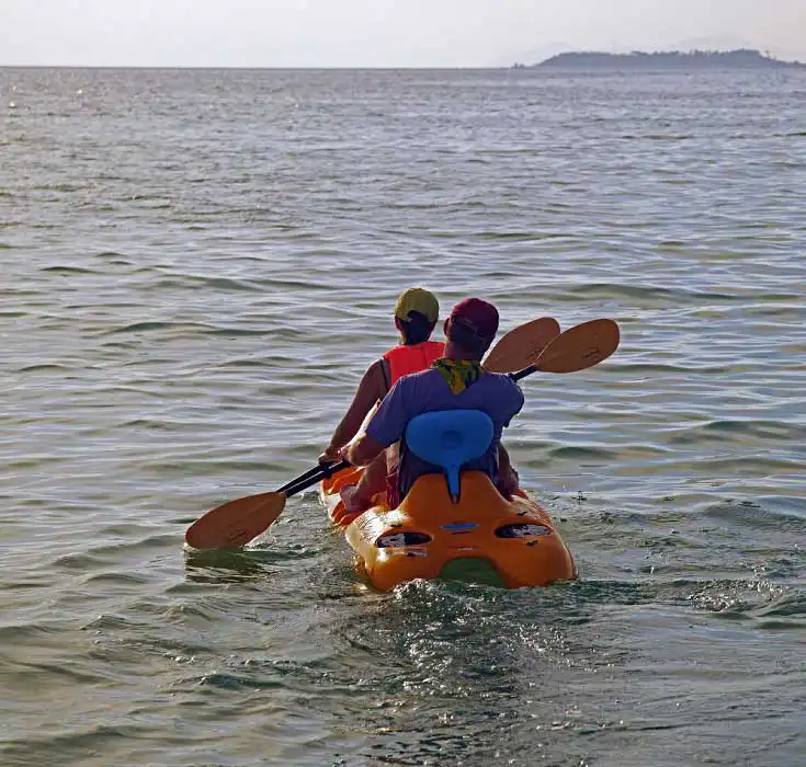 Couple of guests on a brightly colored yellow sea kayak exploring the calm turquoise waters with mabul island in the distant backgroun.