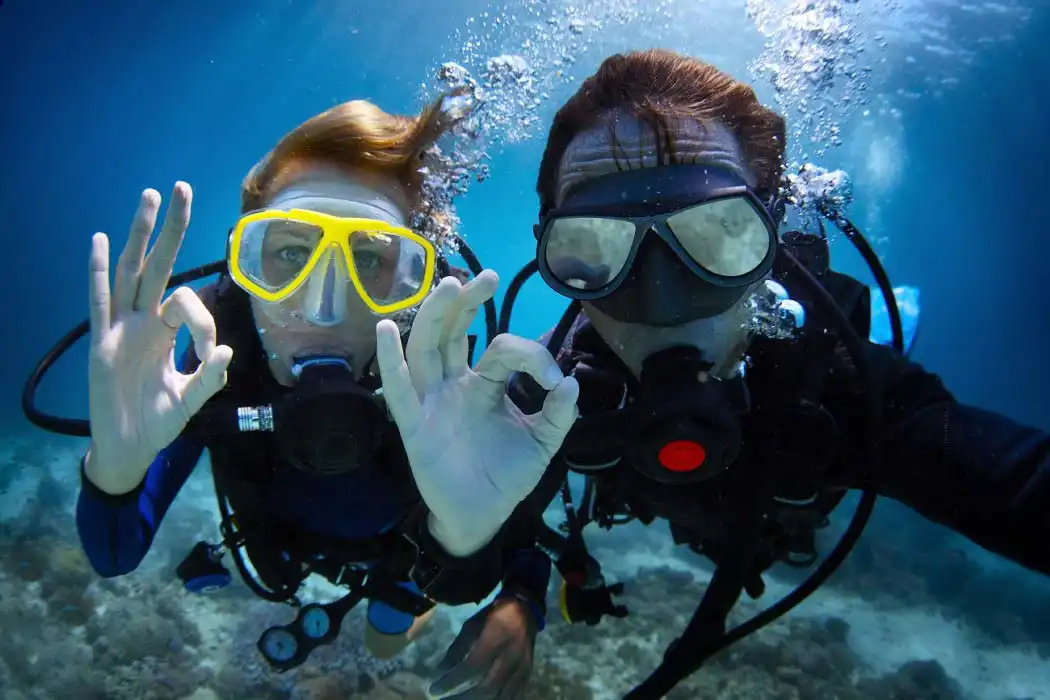 Happy scuba diver giving the 'OK' hand signal underwater, surrounded by blue water and healthy coral reef at Mabul island.