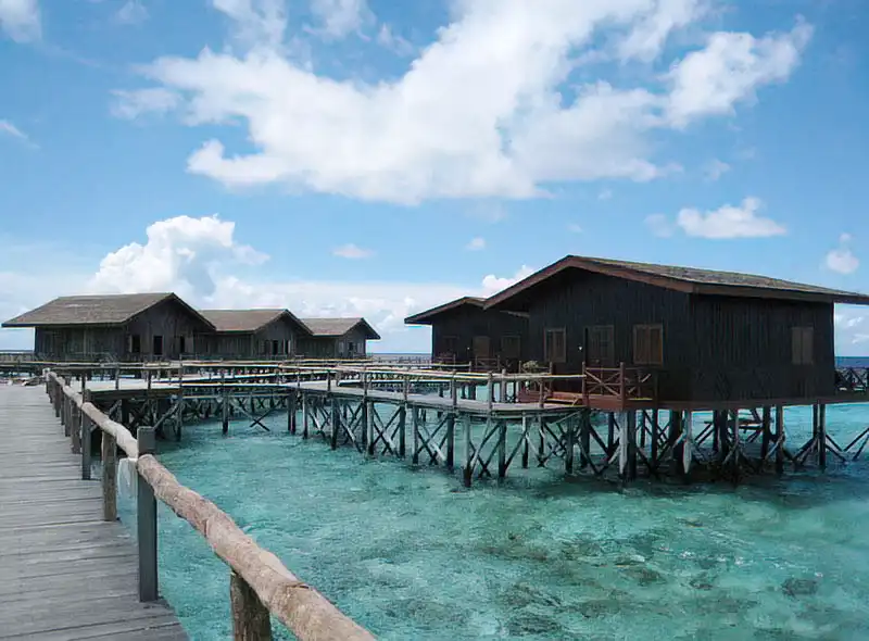 Luxurious overwater villas at Pom Pom Island Resort, connected by a wooden jetty over the crystal-clear turquoise reef of the Celebes Sea, perfect for a 5-star honeymoon.