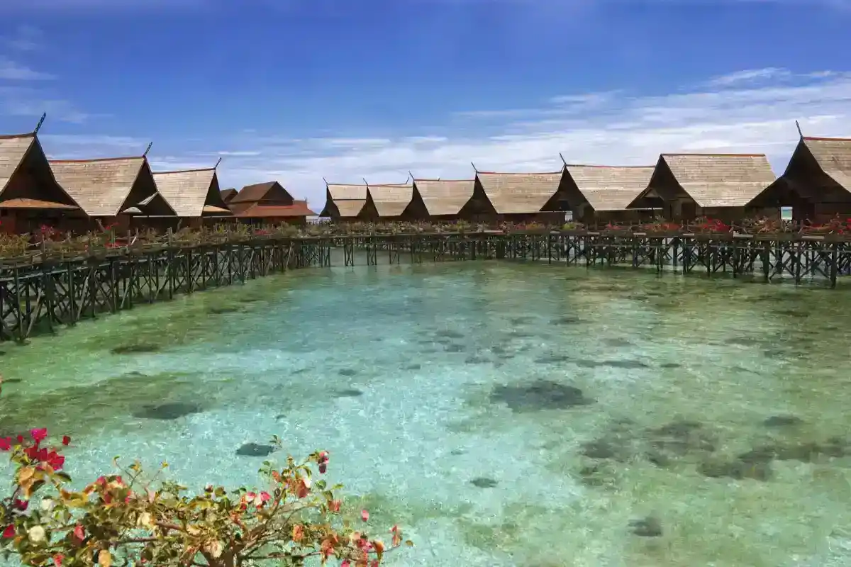 Iconic wooden overwater chalets of the Kapalai Water Village resort, standing in the crystal-clear turquoise sea under a blue sky.