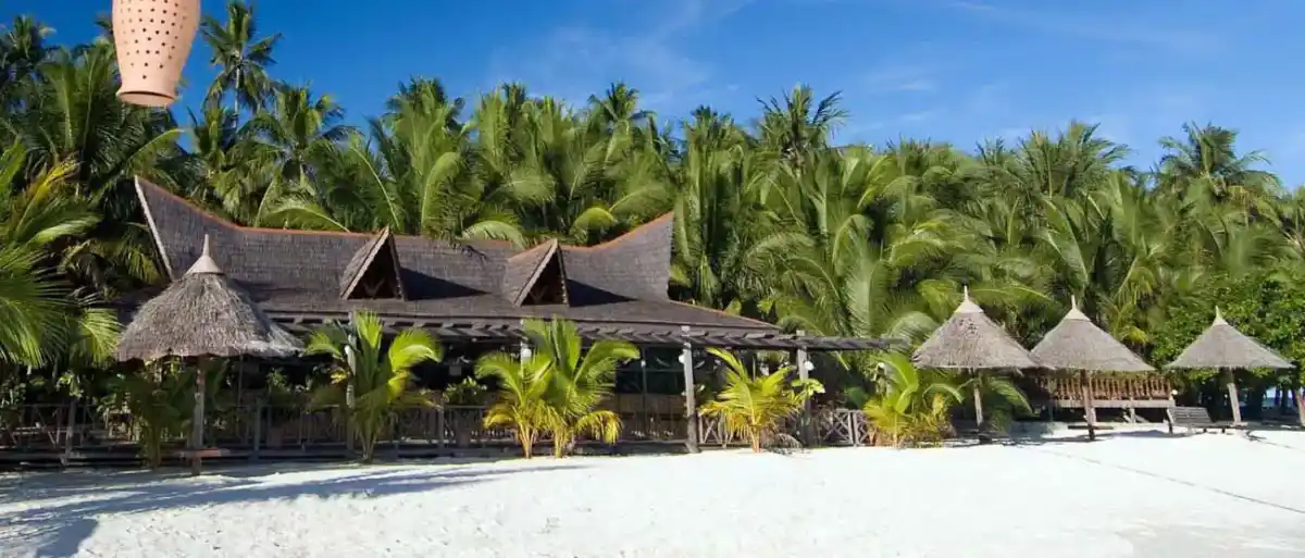 Panoramic view of the beautiful Sipadan-Mabul Resort, with its main building and thatched-roof gazebos nestled against a forest of palm trees in front of the beach.
