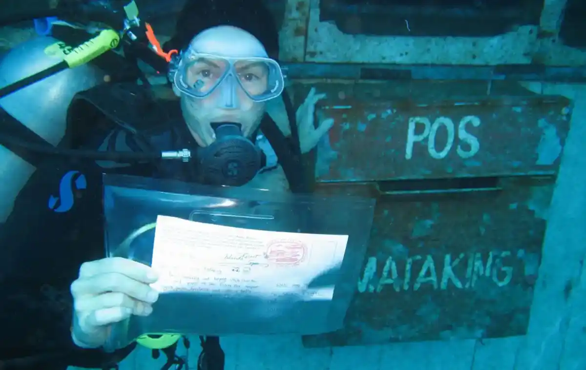 A scuba diver 'mailing' a postcard at the unique Underwater Post Office at Mataking Island, a fun novelty for a 5-star diving holiday.